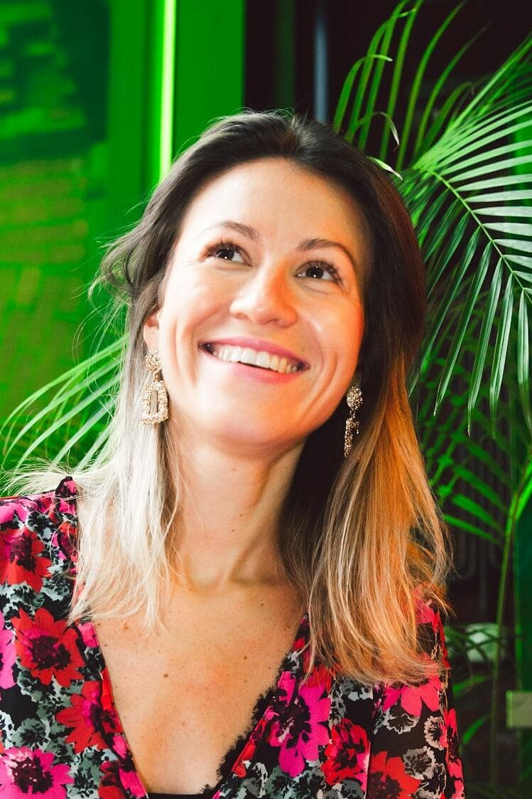 Smiling woman using a laptop in a modern indoor setting with lush greenery.